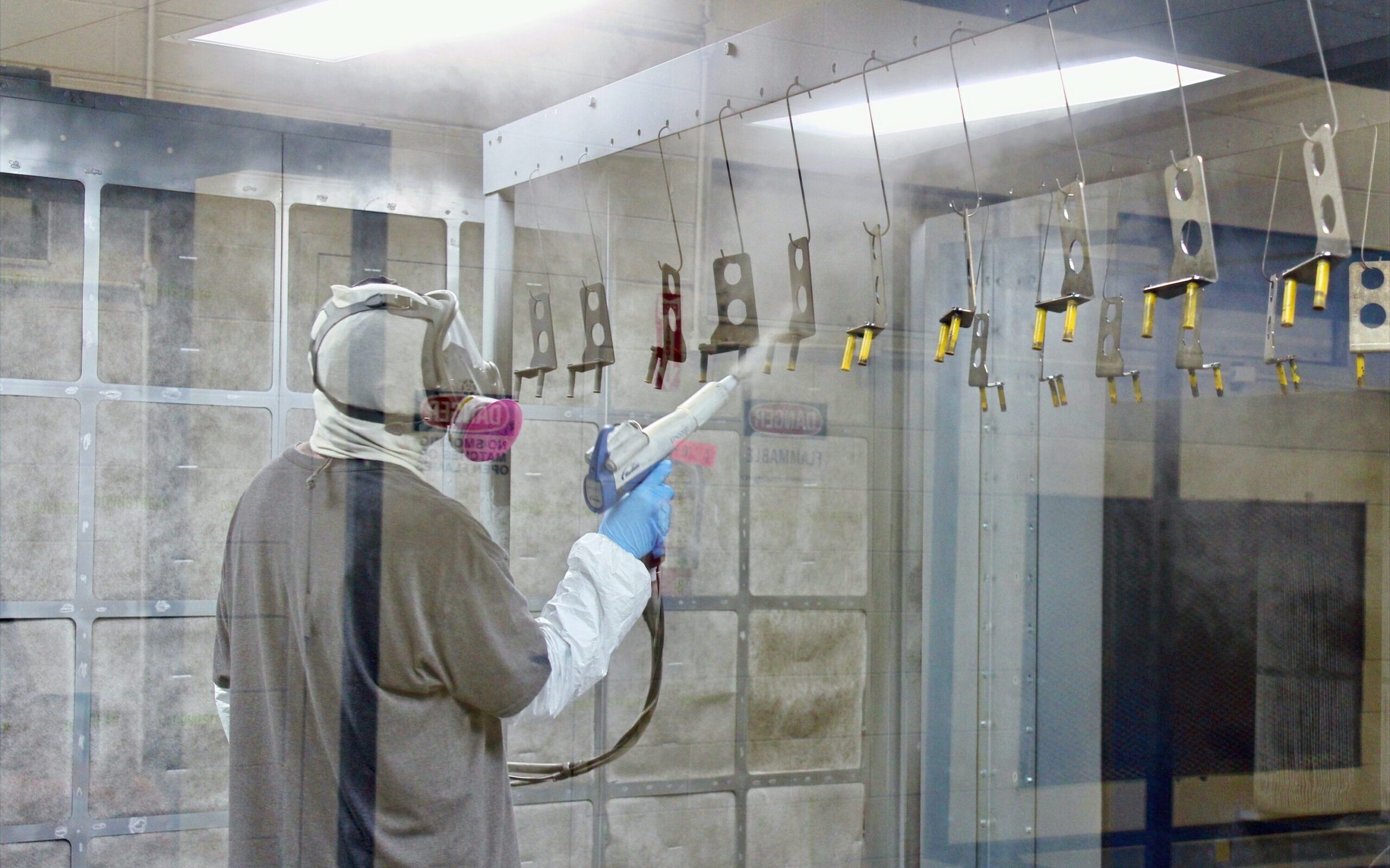 A photo of a person in safety gear using a device to powder coat several parts